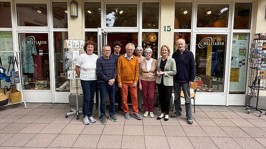 Mehrere Frauen und Männer stehen gemeinsam im Freien vor der Fensterfront eines Geschäfts.