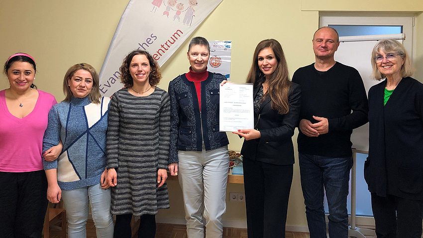 Eine Gruppe von vielen Personen steht zusammen und hält einen Zettel in die Kamera.