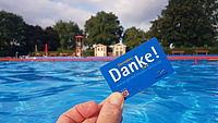 Eine blaue Karte mit der Aufschrift "DANKE". Im Hintergrund ein Freibad.