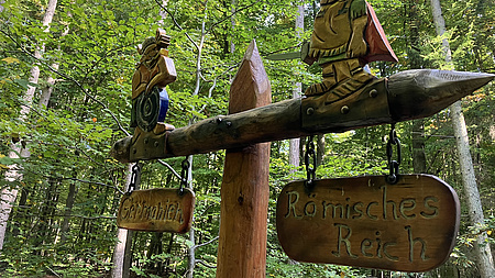 Zu sehen sind hölzerne Hinweisschilder in einem Wald.