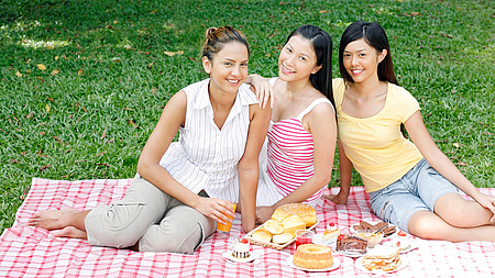 drei junge Frauen sitzen auf einer Picknickdecke, davor etwas zu essen