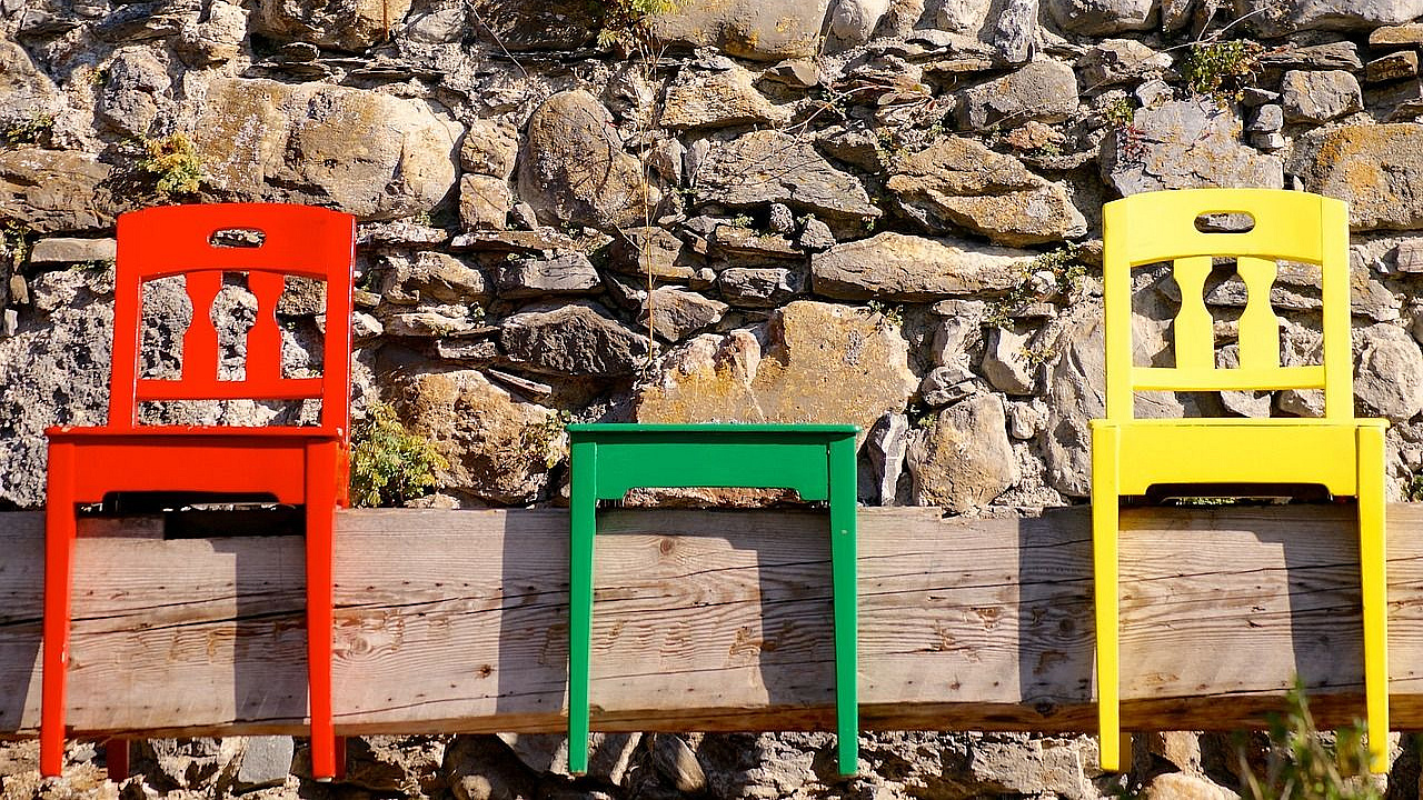 Zwei bunte Stühle und ein Hocker auf einem Holzbalken