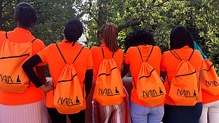 6 schwarze Mädchen sind von hinten zu sehen, sie tragen Rucksäcken mit der Aufschrift Nala e.V.