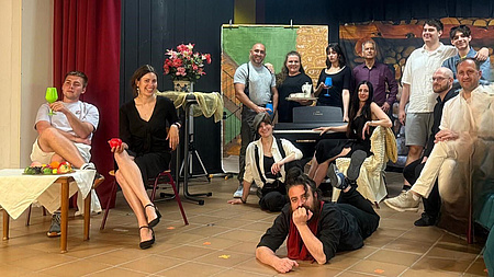 Eine Gruppe Menschen vor einer gemalten Kulisse sitzend, stehend und liegend