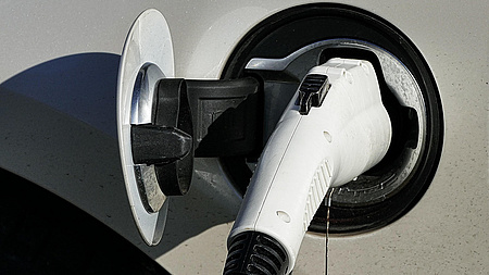 Der Ladestecker einer E-Ladestation steckt in der Ladebuchse eines Elektrofahrzeugs.