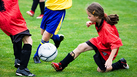 Drei Fußballspielerinnen im Spiel, davon ein Mädchen mit dem Ball knieend