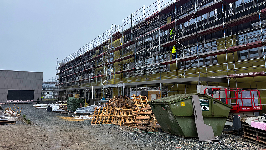 Ein im Bau befindliches Gebäude. Rundherum sind Gerüste aufgebaut. Mehrere Arbeiter sind zu sehen.