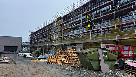Ein im Bau befindliches Gebäude. Rundherum sind Gerüste aufgebaut. Mehrere Arbeiter sind zu sehen.