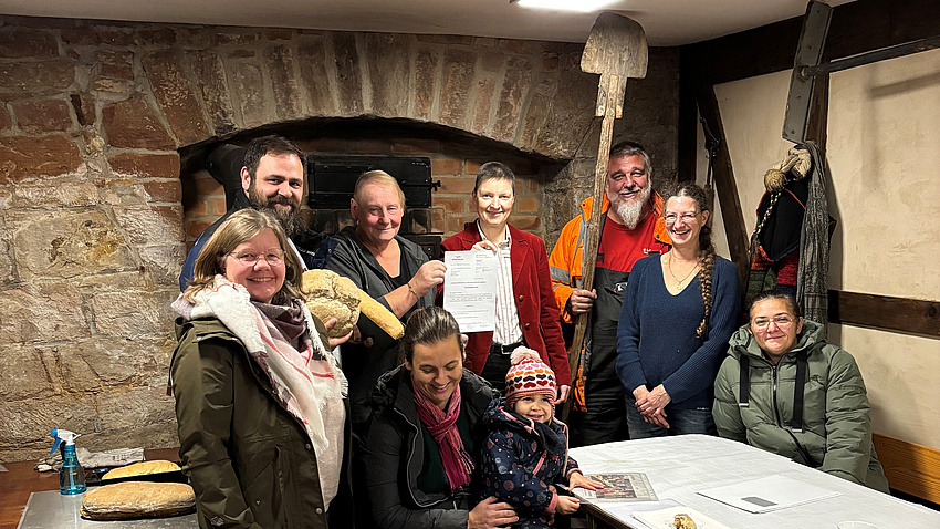 Eine Gruppe Menschen steht vor einem alten steinernen Ofen.