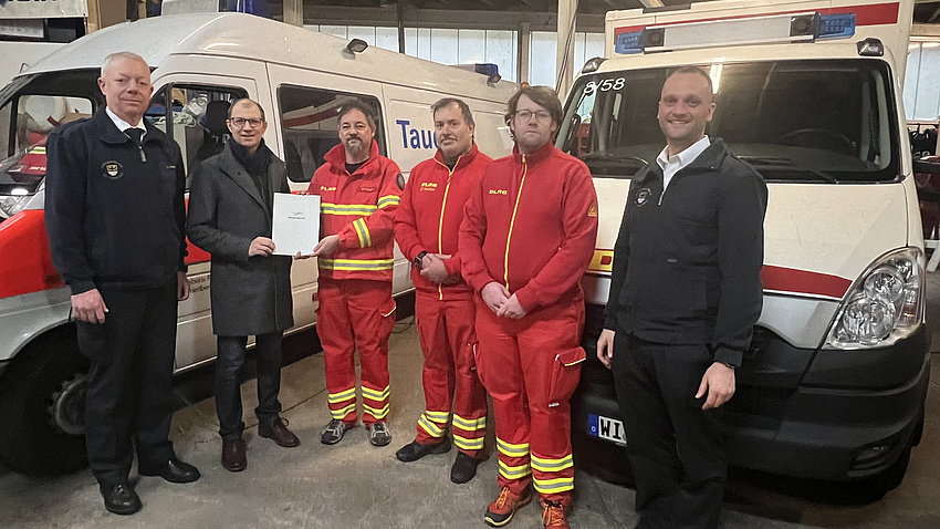 Sechs Männer stehen vor zwei Einsatzwagen. Sie präsentieren ein Dokument.