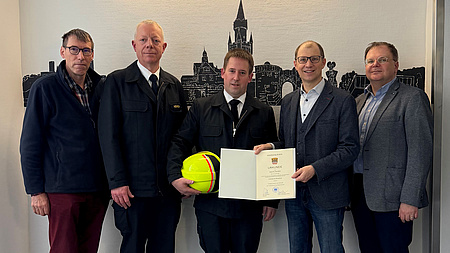 Fünf Männer stehen in einer Reihe. Der neue Kreisbrandmeister in der Mitte bekommt seine Urkunde überreicht.