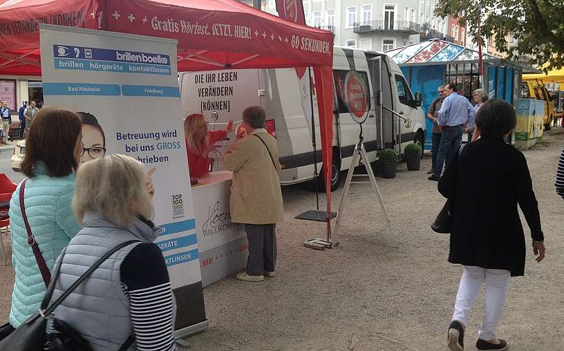 Ein Zelt auf einem Kiesweg. Daneben ein, Aufstelle, der über die Möglichkeit zum Hörtest informiert.