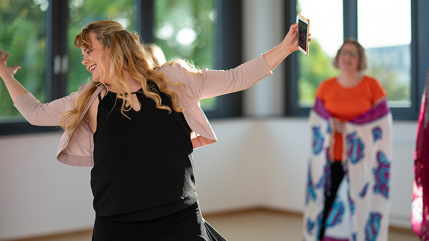 Eine Frau tanzt und lacht mit einem Handy in der Hand