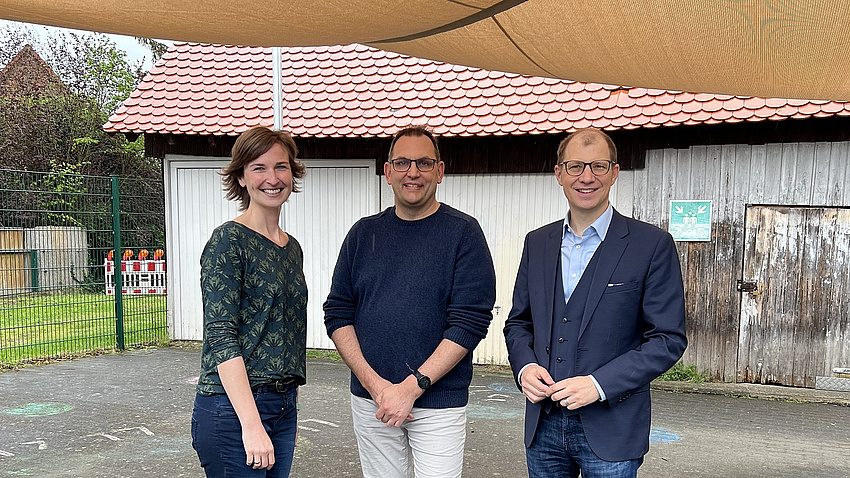 Eine Frau und zwei Männer stehen unter einem Sonnensegel.