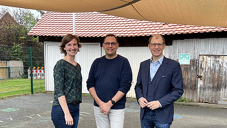 Eine Frau und zwei Männer stehen unter einem Sonnensegel.