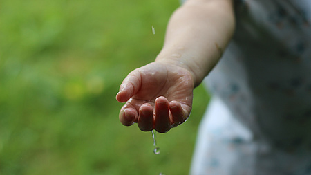 Regentropfen perlen von einer Hand ab.