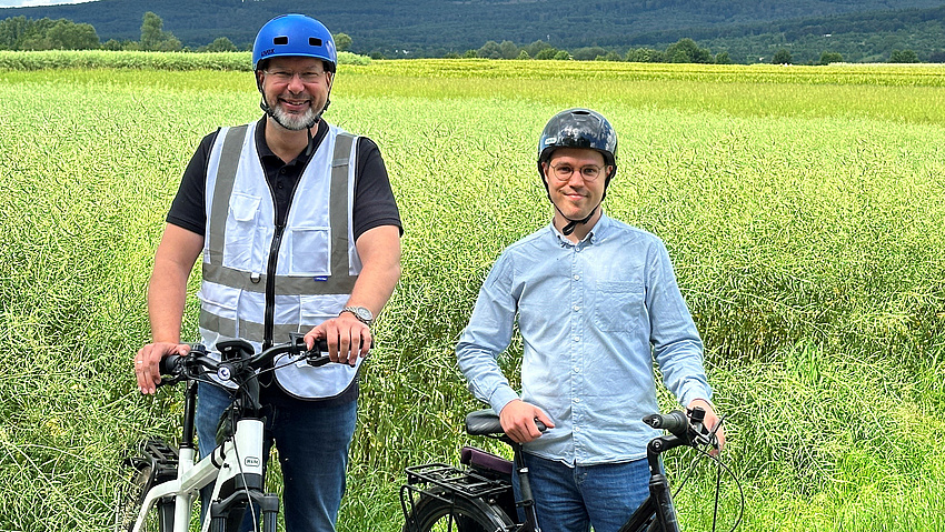 Zwei Männer mit Fahrradhelmen stehe  mit ihren Fahrrädern auf einem Feldweg.