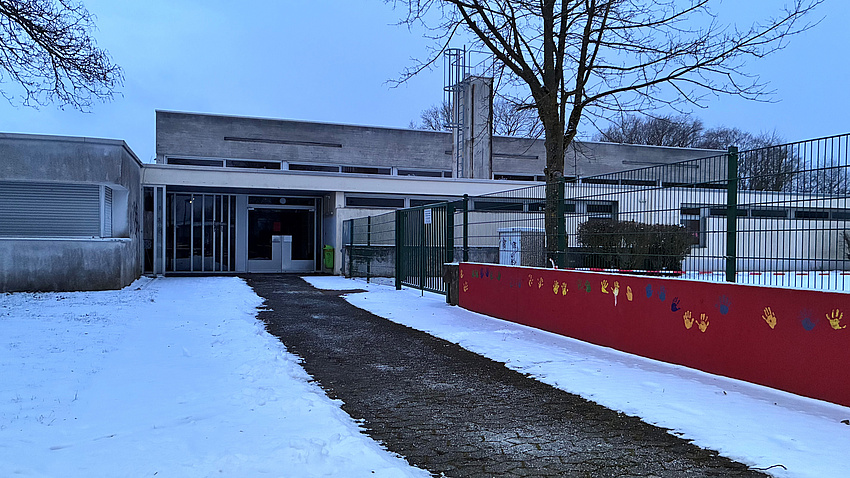 Das Bild zeigt die Sporthalle der Gönser Grund Schule von außen. Wege und Dach sind mit Schnee bedeckt.