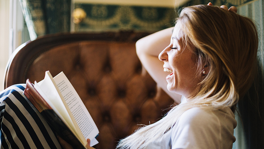 Eine Frau liest ein Buch und lacht dabei herzhaft