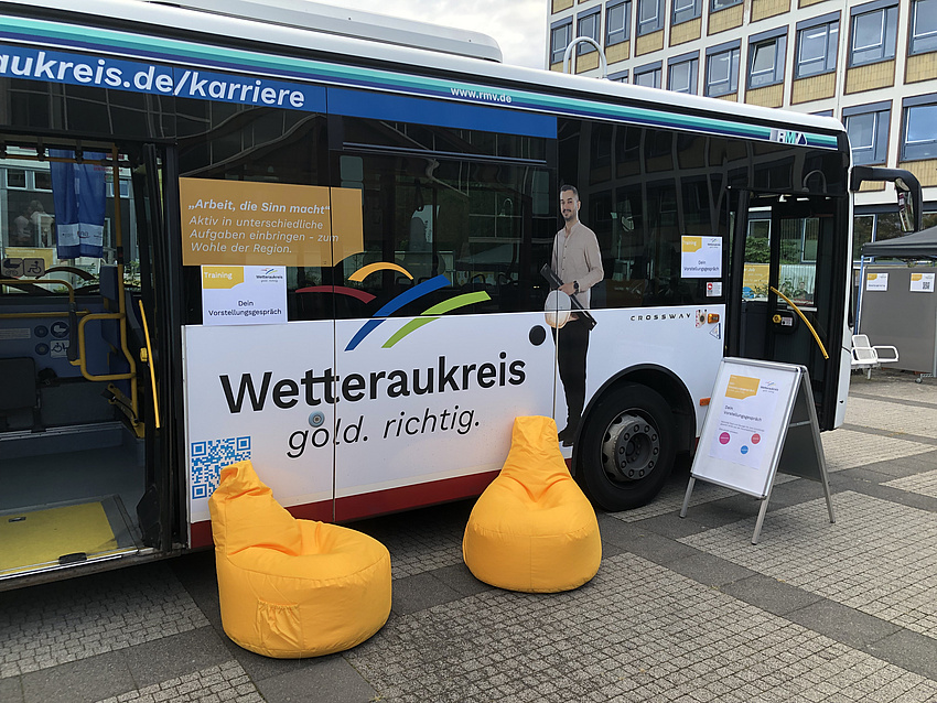 Ein Bus mit der Aufschrift Wetteraukreis gold richtig, aus dem die Jugendlichen informiert werden. Davor zwei gelbe gemütliche Sessel.