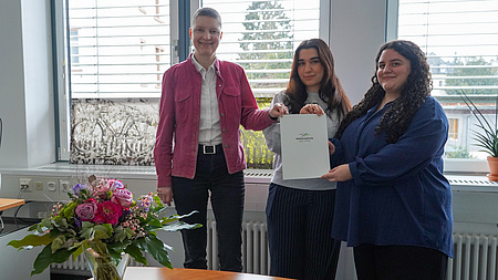 Marion Götz übergibt den Förderbescheid an Beyza-Nur Öz und Meltem Cicek.