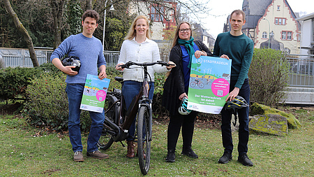 Vier Personen halten Plakate in die Höhe und haben ein Fahrrad zwischen sich stehen.