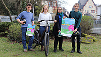 Vier Personen halten Plakate in die Höhe und haben ein Fahrrad zwischen sich stehen.
