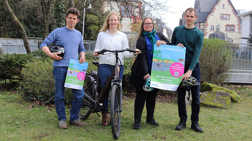 Vier Personen halten Plakate in die Höhe und haben ein Fahrrad zwischen sich stehen.