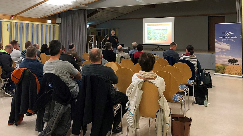 Ein Saal voller Leute lauscht einem Referenten.