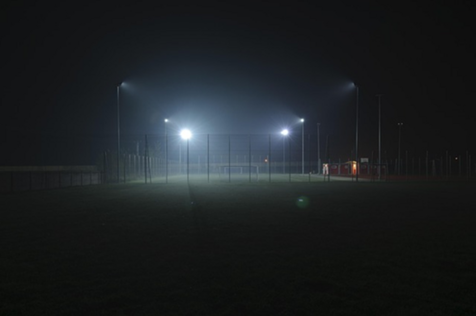 Hell strahlende Flutlichter an Masten auf einem Sportgelände
