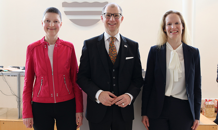 Ein Mann und zwei Frauen stehern nebeneinander und lächeln in die Kamera.