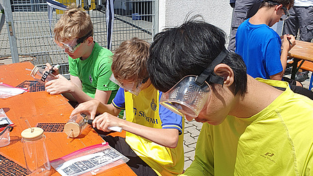 Drei Jungen, die auf Bänken sitzen und mit Gravurstiften Trinkgläser gravieren