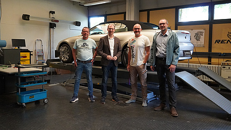 Vier Männer stehen vor einer Hebebühne mit Auto.