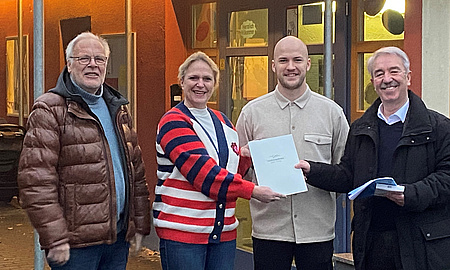 Eine Frau und drei Männer stehen nebeneinander. Zwei Personen halten gemeinsam ein Schriftstück.