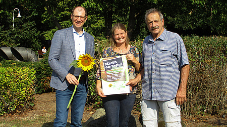Drei Personen halten ein Plakat in der Hand, auf dem "Markt der Region 2024" steht.