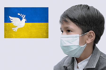 Symbolbild. Eine Ukrainefahne, daneben ein Kind, das einen Mund-Nasenschutz trägt