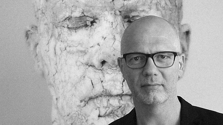 Ein Mann steht vor einem Gemälde, das einen Kopf zeigt, dessen Haut zerbröckelt.