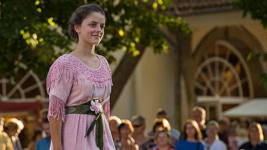 Eine junge Frau in historischer Jugendstil-Bekleidung. Im Hintergrund Publikum.