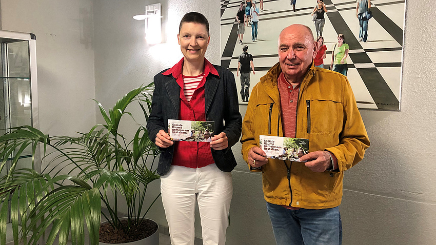 Sozialdezernentin Marion Götz und Kreisbeigeordneter Bardo Bayer halten einen Flyer in die Kamera.