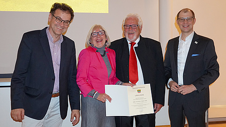 Landrat Jan Weckler (rechts) und Kreistagsvorsitzender Armin Häuser (links) überreichen die Urkunde an Gaby und Hans-Jürgen Zeeb.
