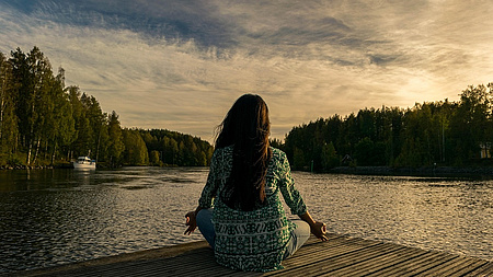 Eine Frau am See auf einem Steg von hinten in der Abendsonne