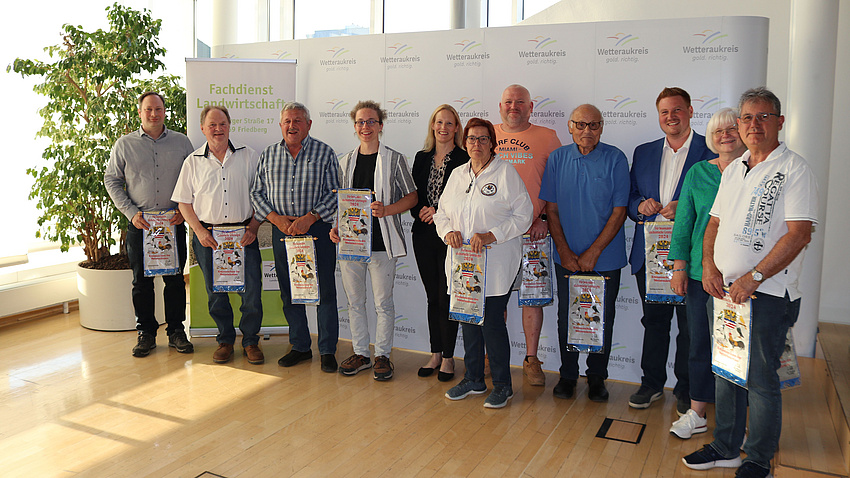 Mehrere Frauen und Männer stehen in einem Saal vor einer Stellwand und halten Wimpel in der Hand.