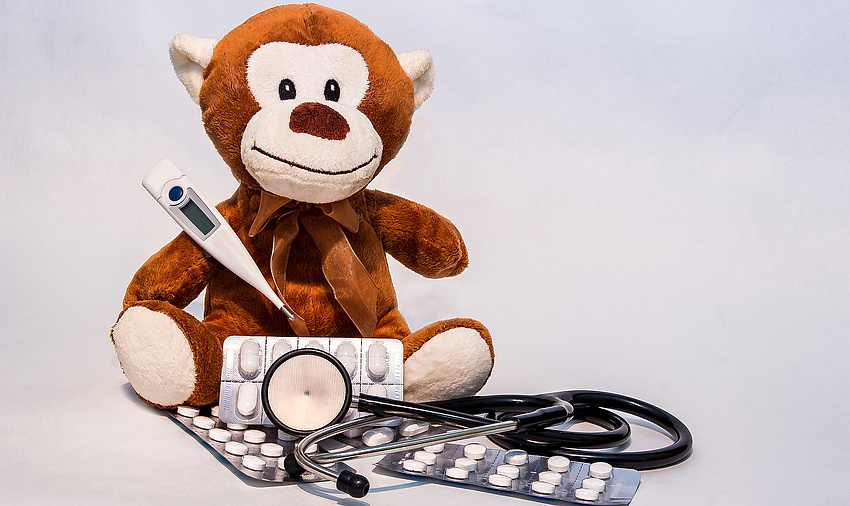 Ein Pläschäffchen. Vor ihm ein digitales Fieberthermometer, Tabletten in einer Durchdrückpackung und ein Stethoskop.