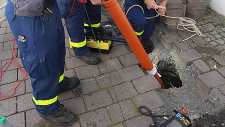 Personen mit blauer Uniform untersuchen ein Loch im Boden.