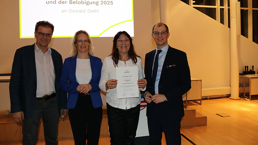 Auf dem Bild sind vier Personen zur sehen. Sie feiern die Verleihung des Umweltschutzpreises des Wetteraukreises, die Preisträgerin hält ihre Urkunde in der Hand.