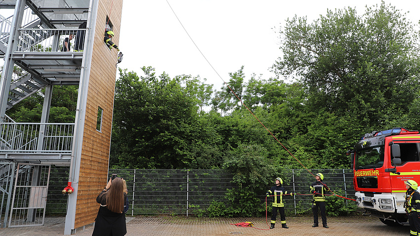 Auf dem Bild ist ein Metallturm zu sehen, an dem Feuerwehrleute das Abseilen üben.