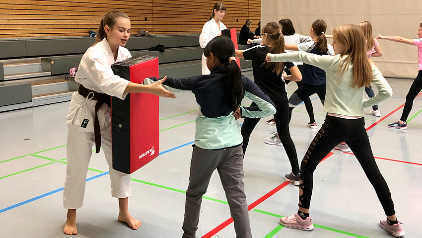 Mädchen üben Karate. Sie stehen sich in Kampfstellung gegenüber.