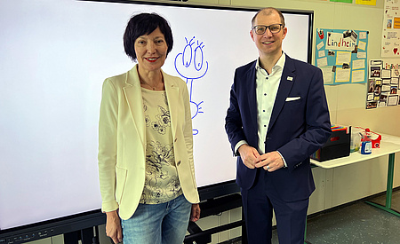 Ein Mann und eine Frau stehern vor einer weißen Schultafel