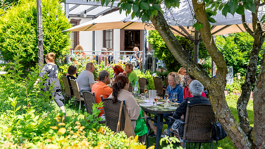 Menschen, die im Garten an einem langen Tisch sitzen.