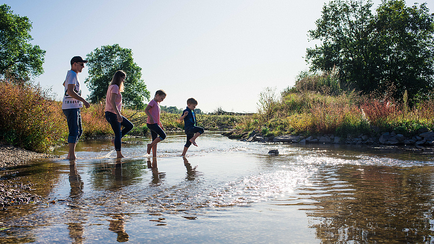 Eine Familie watet durch einen seichten Fluss.